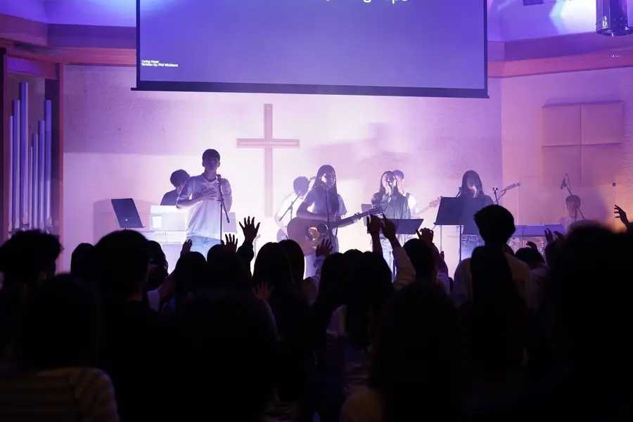 Student worship band leading under purple stage lights with the cross behind them