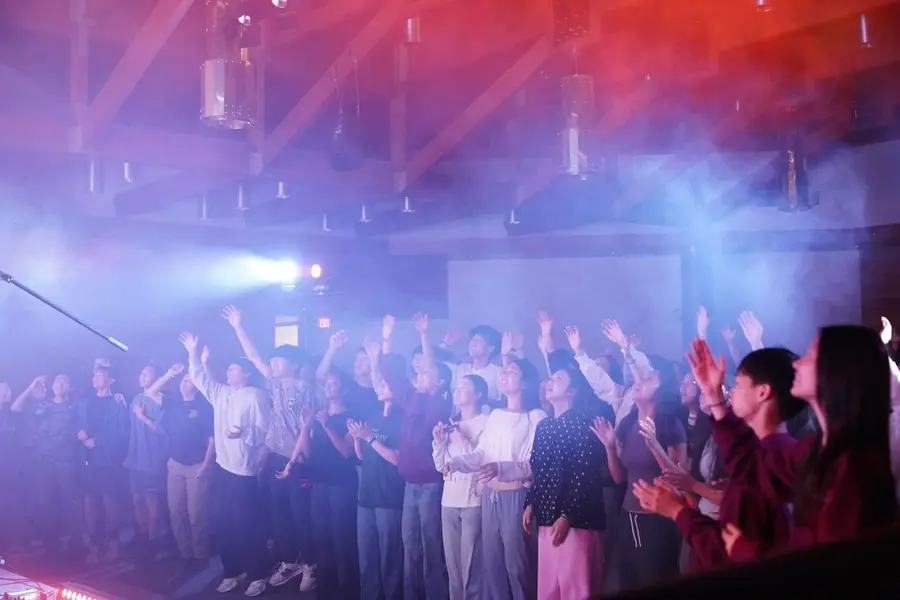 Crowd of students with hands raised in haze and colored light